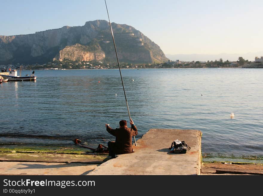 Old man fishing in the port of Mondello, near Palermo. Coast line, mont and beach. Sicily - Italy