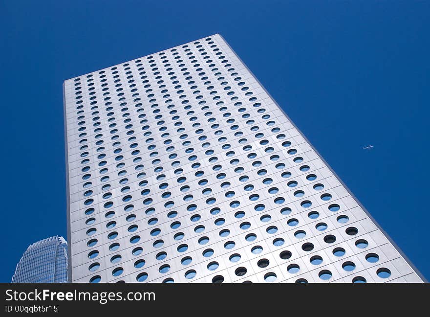 Looking up the skyscrapers in hong kong on a clear blue cloudless day a plane flys past