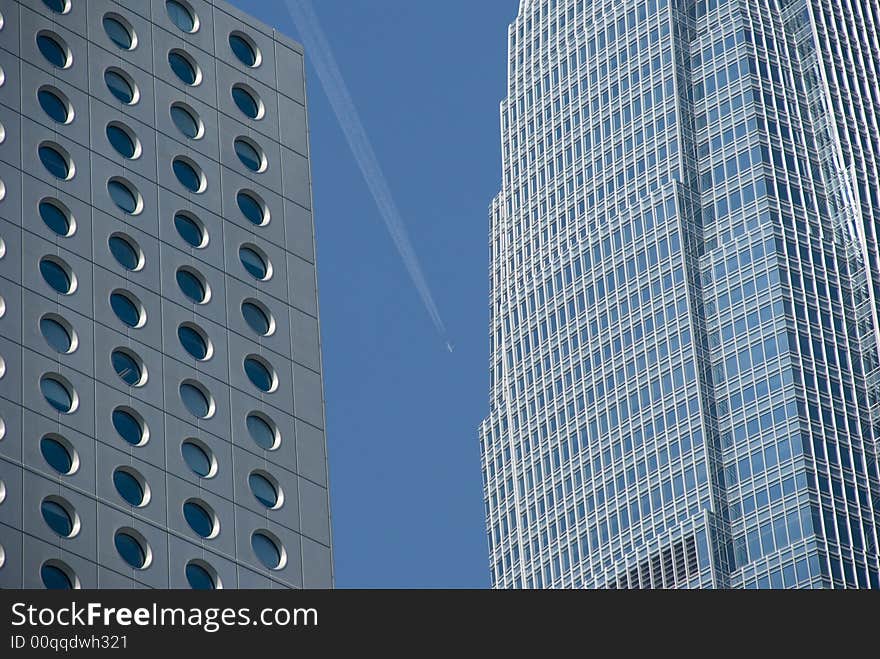 A plane flys past hong kong sky scrapers leaving a vapour trail to mark its path