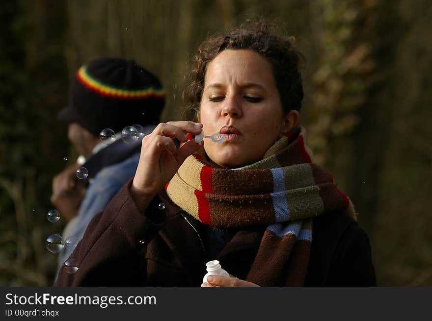 Portrait of a young woman making soap bubbles and a guy in background.