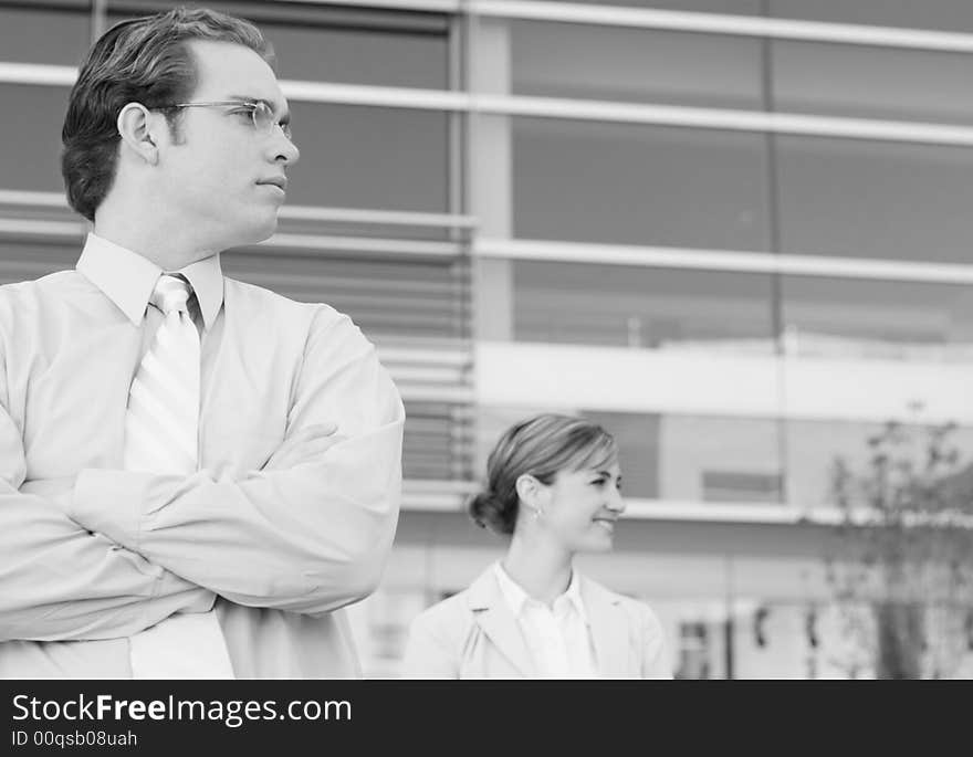 Two people standing looking to their left in front of office building, woman smiling. Two people standing looking to their left in front of office building, woman smiling