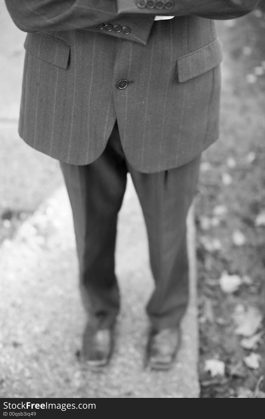 Waist-down front shot of businessman folding arms wearing suit standing on sidewalk. Waist-down front shot of businessman folding arms wearing suit standing on sidewalk