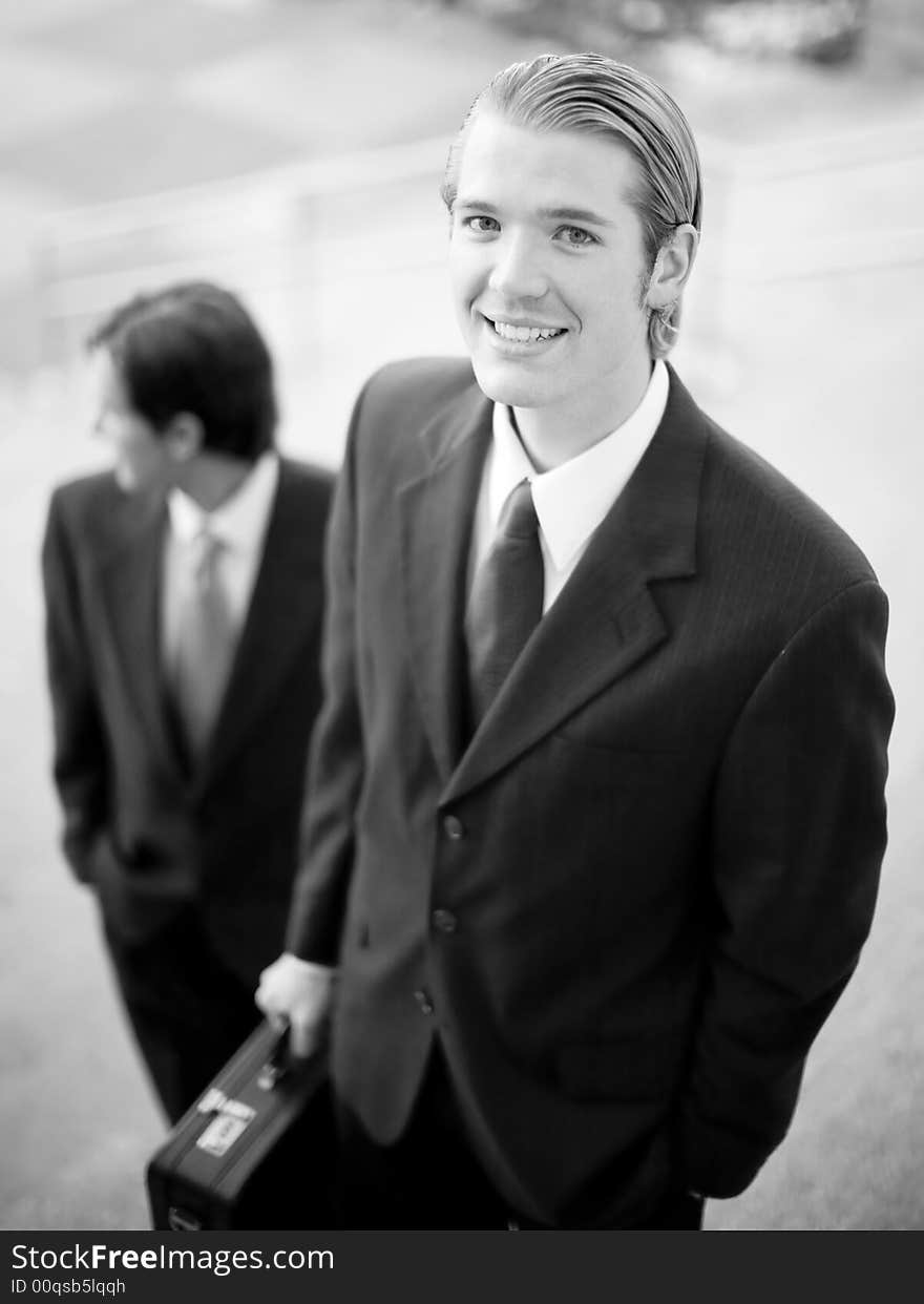 Two businessmen standing on steps in suits holding briefcase looking up while other is looking away