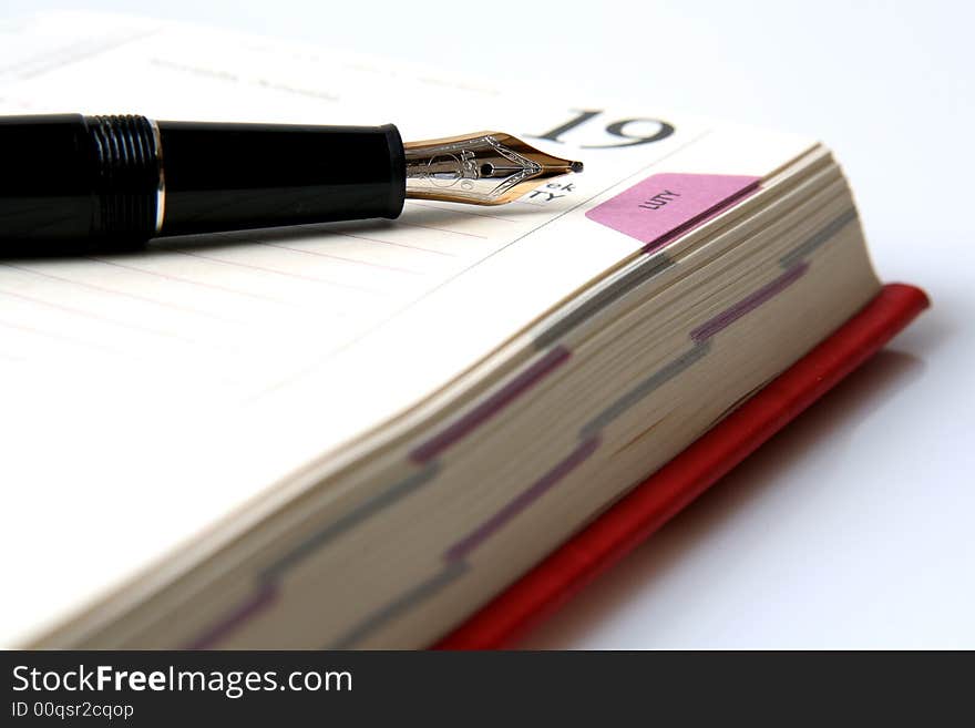 Gold and  black fountain pen on the opened diary on a light background. Gold and  black fountain pen on the opened diary on a light background