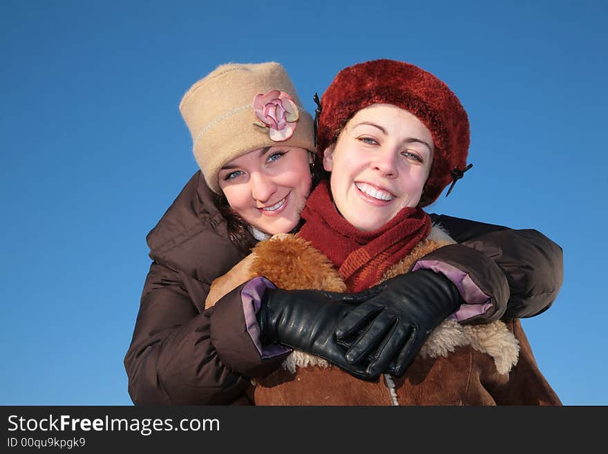 Young woman embraces other against blue sky in winter