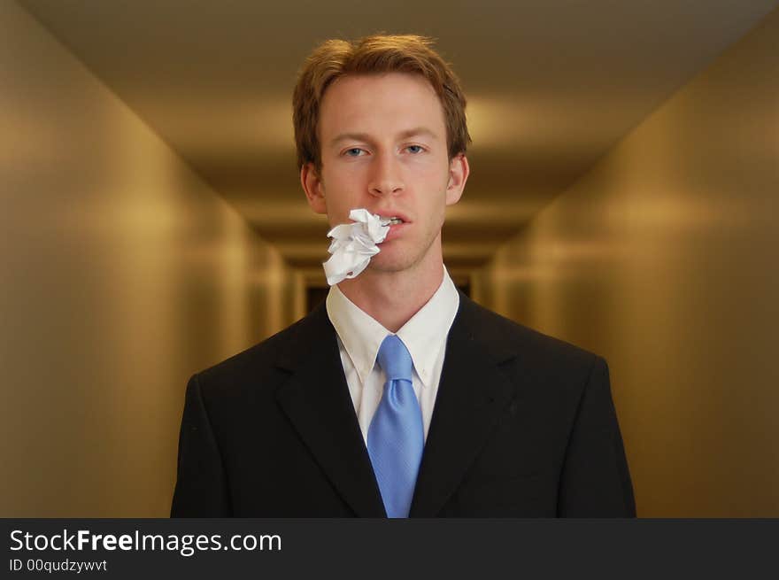 A man in a black suit stands in an empty hallway with a crumpled piece of paper in his mouth. A man in a black suit stands in an empty hallway with a crumpled piece of paper in his mouth