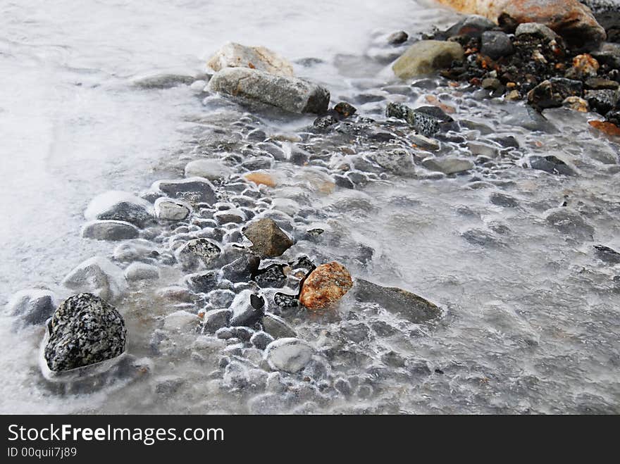 A frozen river stream with colorful stones under it. A frozen river stream with colorful stones under it