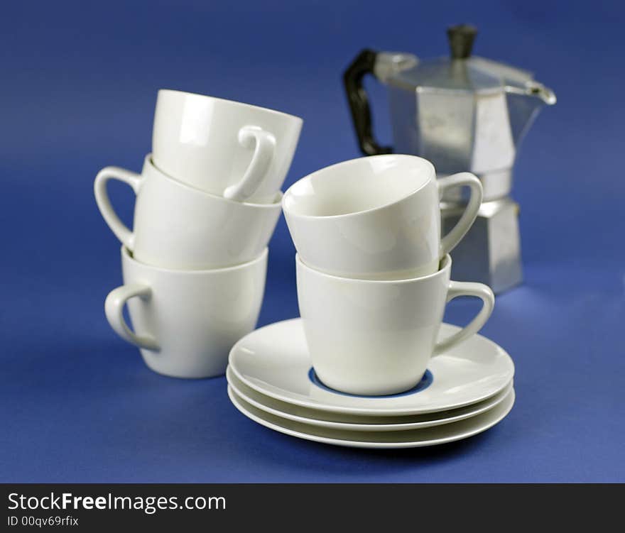 Espresso coffee cups, saucers and espresso machine on blue ground; differential focus