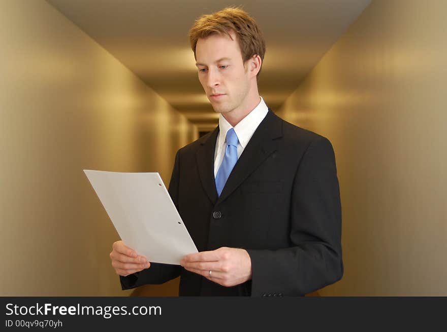 A young man in a black suit stands in an empty looking at a piece of paper. A young man in a black suit stands in an empty looking at a piece of paper