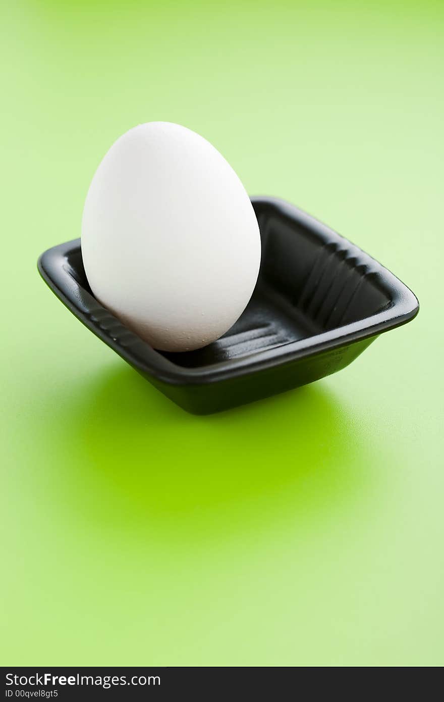 White egg on the small black cup over a green background