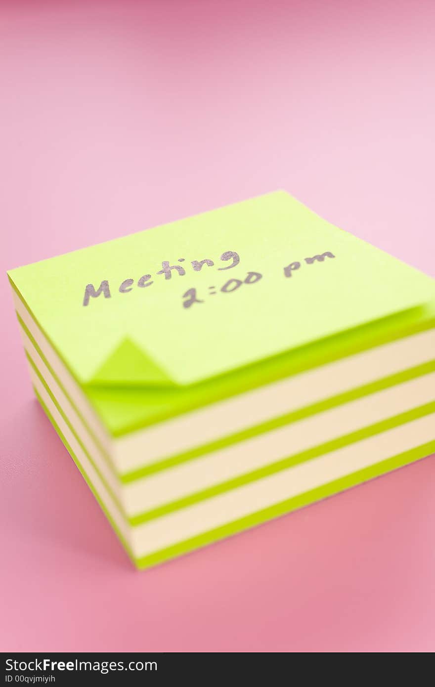 Pile of sticky notes with meeting reminder text over a pink table