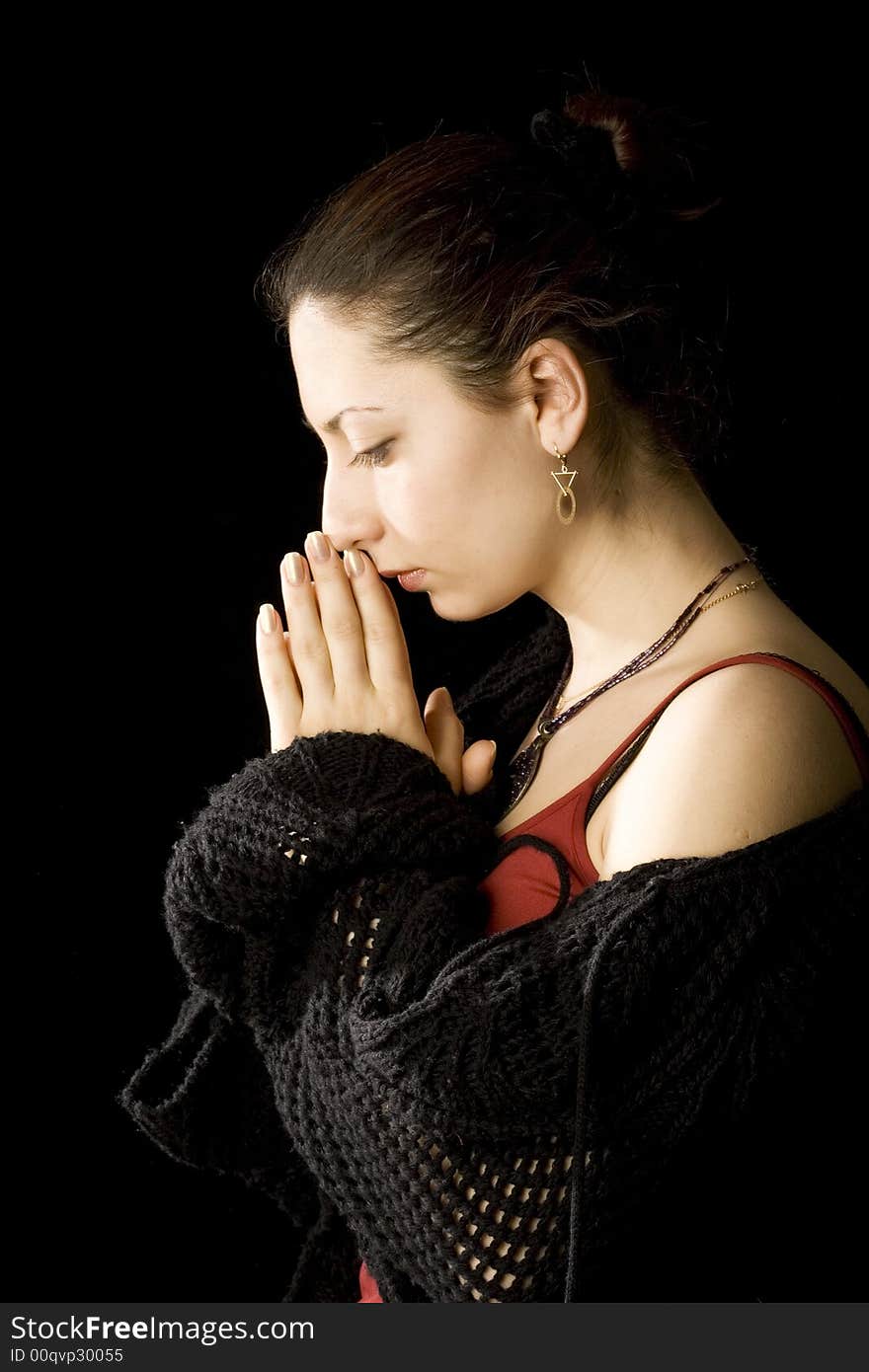 Portrait of young beautiful woman on black background. She stand sideview to a viewer with closed eyes and humbly hold palms near face like  offering up a prayer. Portrait of young beautiful woman on black background. She stand sideview to a viewer with closed eyes and humbly hold palms near face like  offering up a prayer