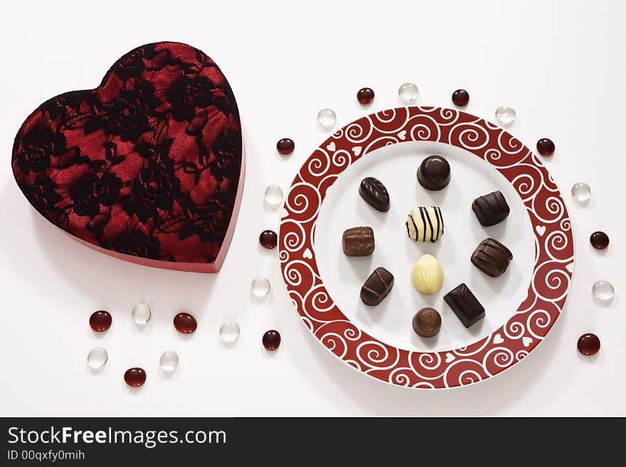 A plate of Valentine's Day chocolates with a heart shaped box on a white table decorated table jewels. A plate of Valentine's Day chocolates with a heart shaped box on a white table decorated table jewels.