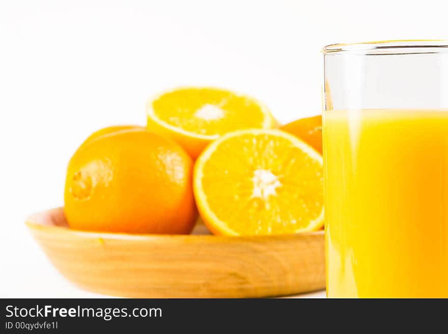 Two halves of orange in a wooden bowl with uncut oranges and a glass of orange juice in the foreground