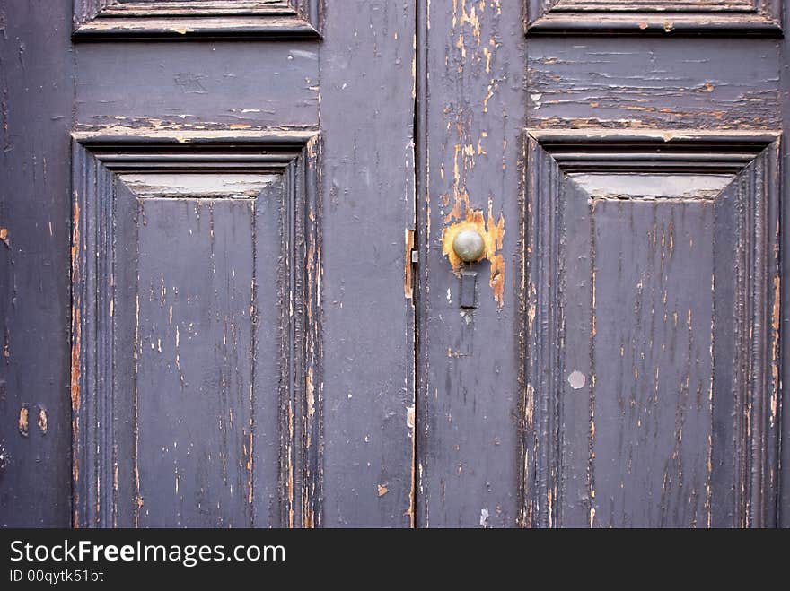 Old double door with peeling cracked paint, a brass door knob with all the paint worn from around it. Old double door with peeling cracked paint, a brass door knob with all the paint worn from around it