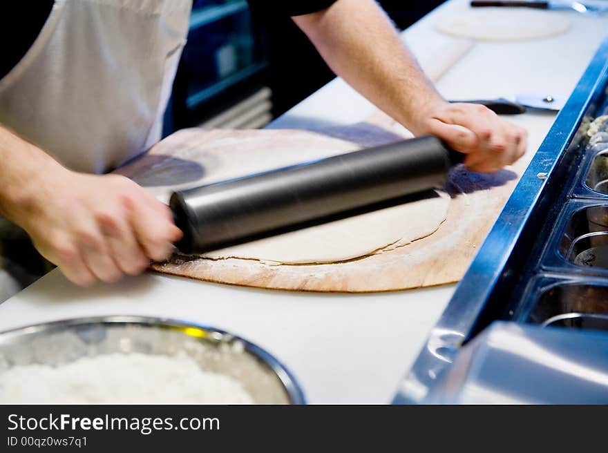 Rolling out dough for pizza with pin in motion. Rolling out dough for pizza with pin in motion