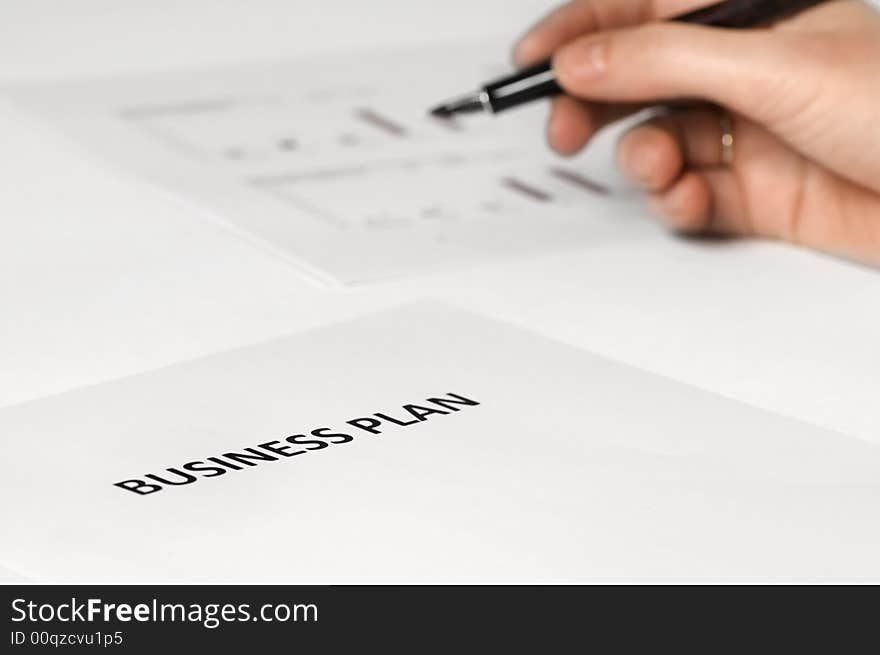 Paper on desk with business plan on it. hand holding pen. paper with graphics on the background. Paper on desk with business plan on it. hand holding pen. paper with graphics on the background.