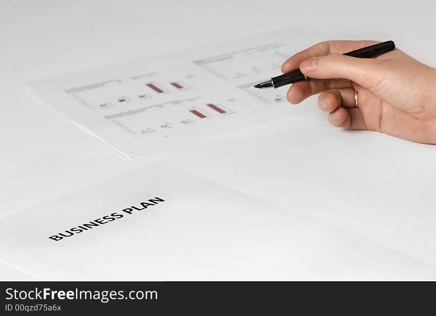 Paper on desk with business plan on it. hand holding pen. paper with graphics on the background. Paper on desk with business plan on it. hand holding pen. paper with graphics on the background.