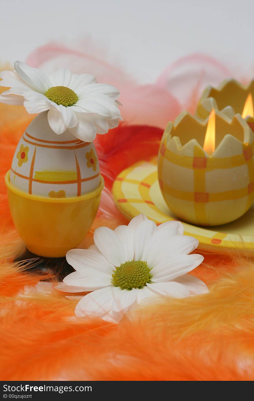 Easter egg and candle with white flowers and pink and orange feathers.