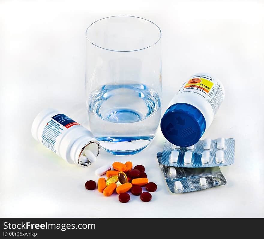 Different pills and vitamins with glass of water over white. Different pills and vitamins with glass of water over white