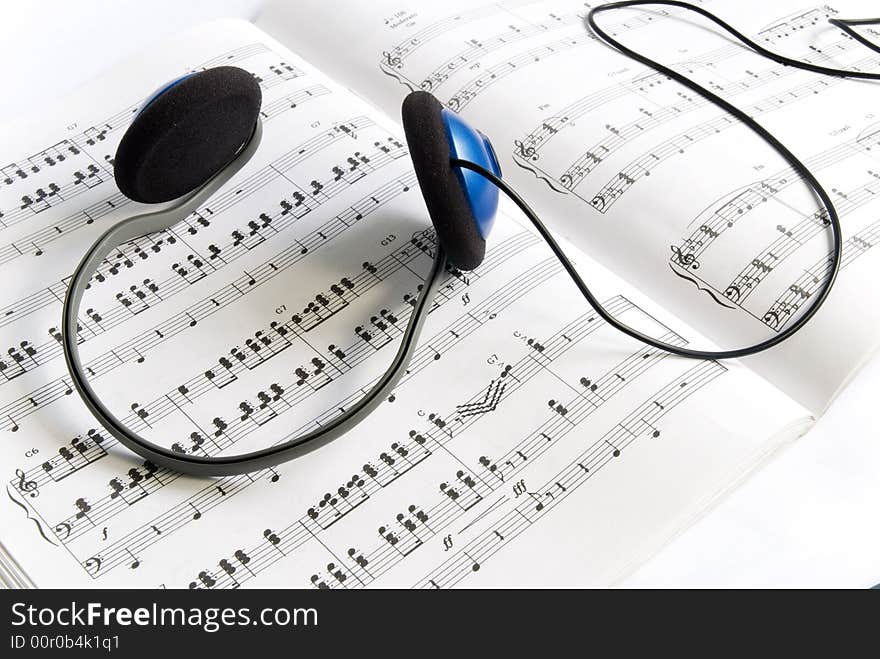 A headphone lying on a book of score sheet. A headphone lying on a book of score sheet