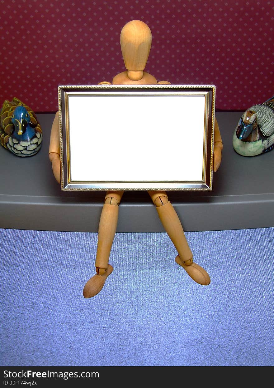 An artist's manikin holding a small picture frame that is blank for text or similar - sitting on a TV set. An artist's manikin holding a small picture frame that is blank for text or similar - sitting on a TV set.