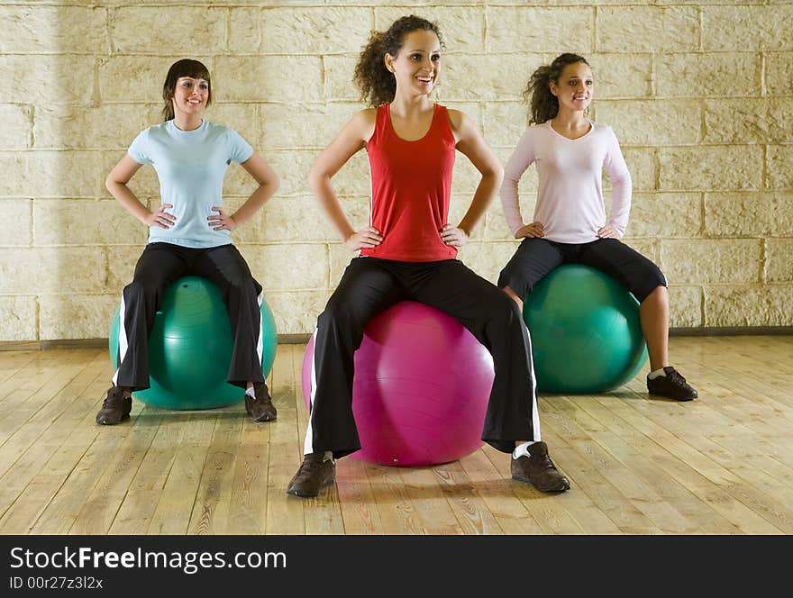 A group of women making exercise sitting on big balls and holding hands on hips. Front view. A group of women making exercise sitting on big balls and holding hands on hips. Front view.