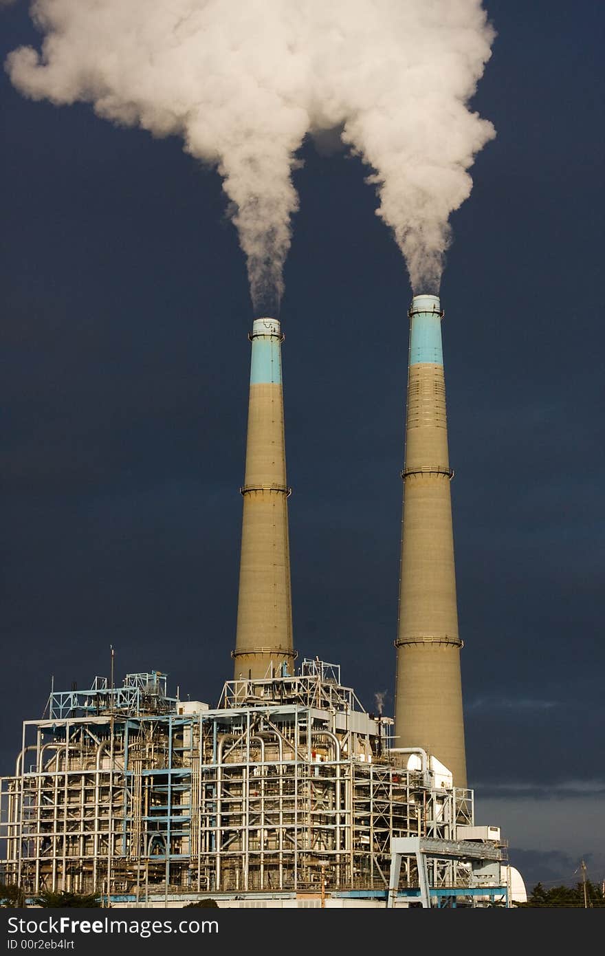 The sun illuminates a power plant in late afternoon while dark clouds roll in behind it. The sun illuminates a power plant in late afternoon while dark clouds roll in behind it