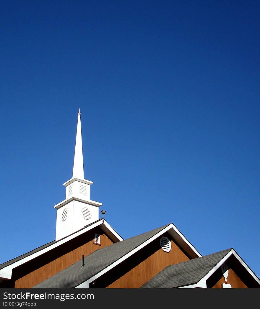 Cross on church roof, three level roof, with blue sky behind.