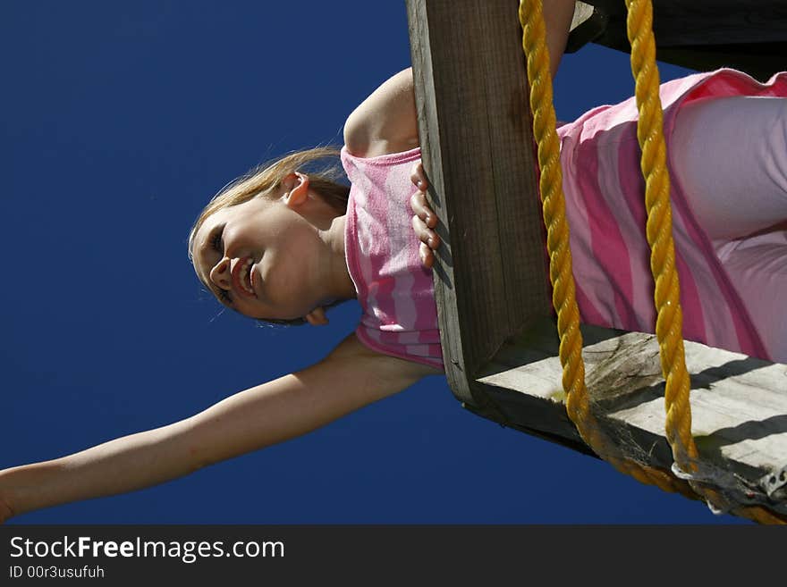 Pretty white caucasian girl playing on a climber on a hot day with blue sky in the background. Pretty white caucasian girl playing on a climber on a hot day with blue sky in the background