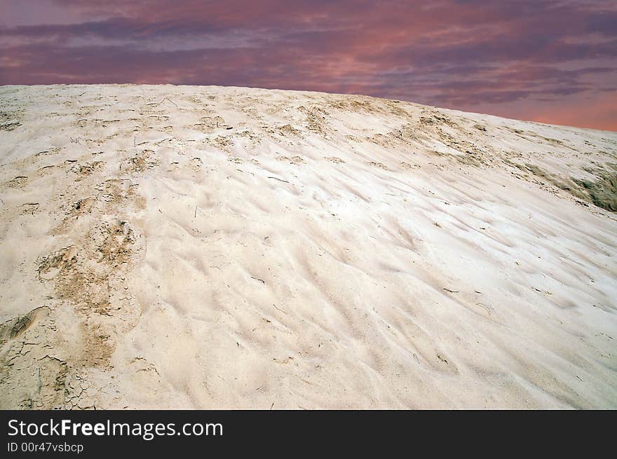 Single pale yellow sand dune with shoe tracks. Sunrise.