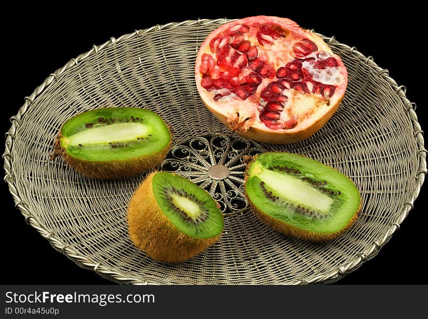 Kivi and pomegranate on a wattled metal tray on a black background. Kivi and pomegranate on a wattled metal tray on a black background