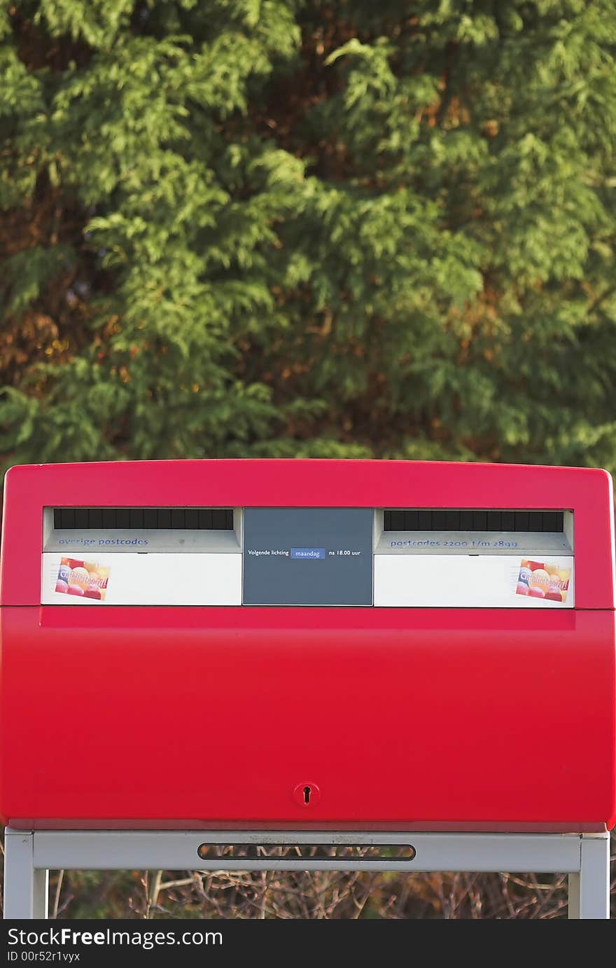 Red dual post box with a green bush in the backgroud