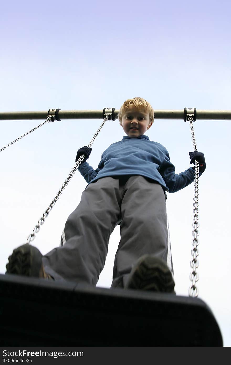 A young boy standing on a swing viewed from below