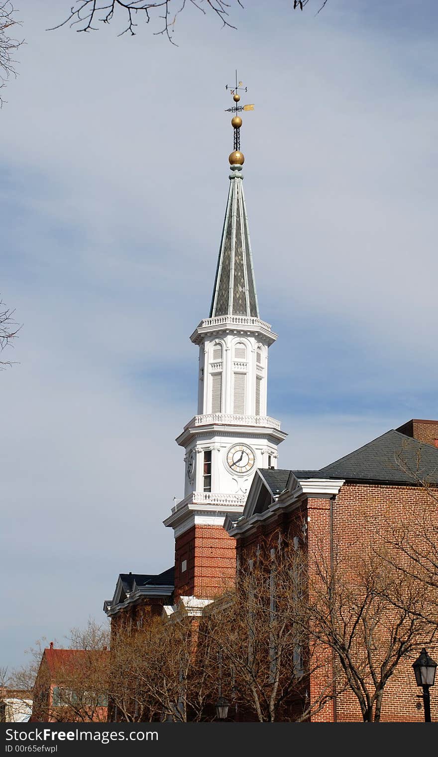 The peaked spike of church looks out of buildings and  trees surrounding it. The peaked spike of church looks out of buildings and  trees surrounding it.