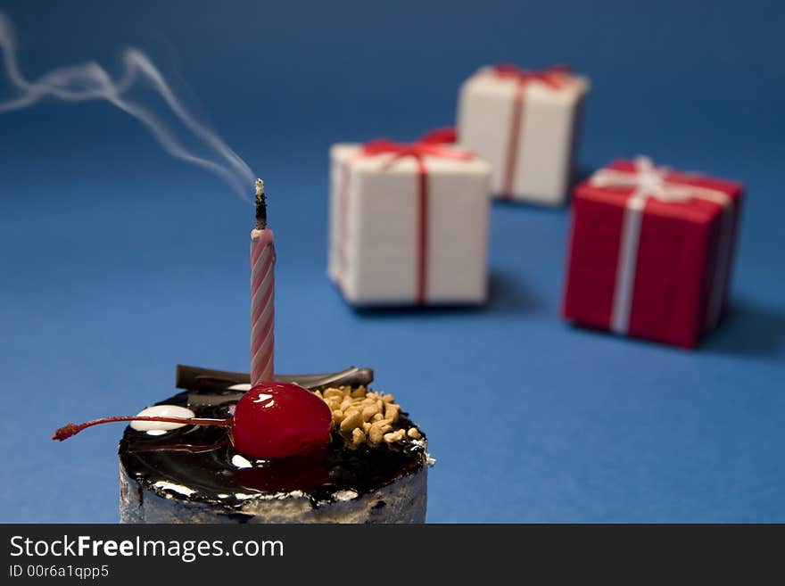 Chocolate cake with candle and gift boxes on blue background. Dessert series. Chocolate cake with candle and gift boxes on blue background. Dessert series.