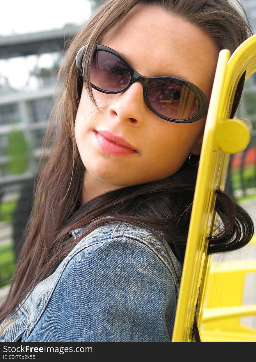 Woman wearing sunglasses seating on a yellow chair