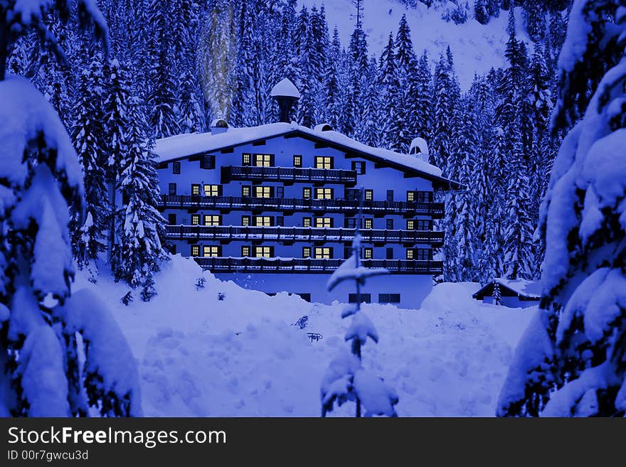 A hotel located in mountains covered by deep snow. Glow of windows and smoke give warm and cozy holiday feeling. A hotel located in mountains covered by deep snow. Glow of windows and smoke give warm and cozy holiday feeling.