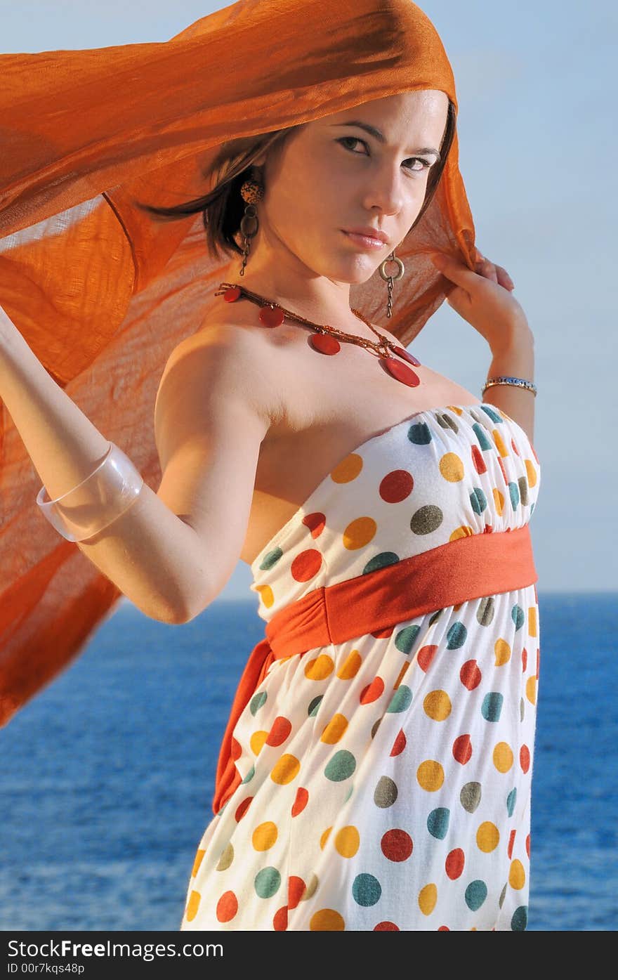 Fashion model holding oragne cloth against ocean background. Fashion model holding oragne cloth against ocean background