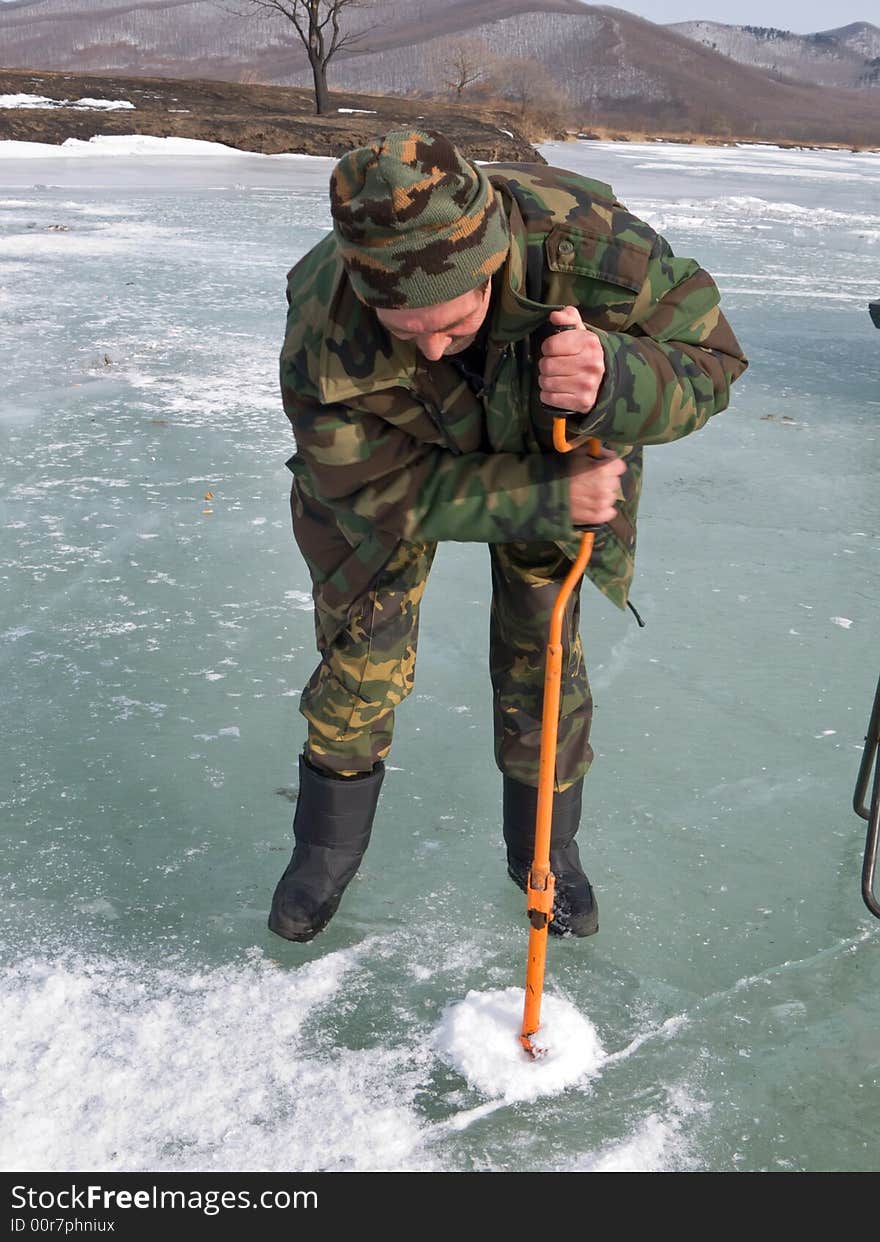 A winter fishing on river. People is fishing the smelt. A man drills a hole in ice. Russian Far East, Primorye, Kievka river. A winter fishing on river. People is fishing the smelt. A man drills a hole in ice. Russian Far East, Primorye, Kievka river.