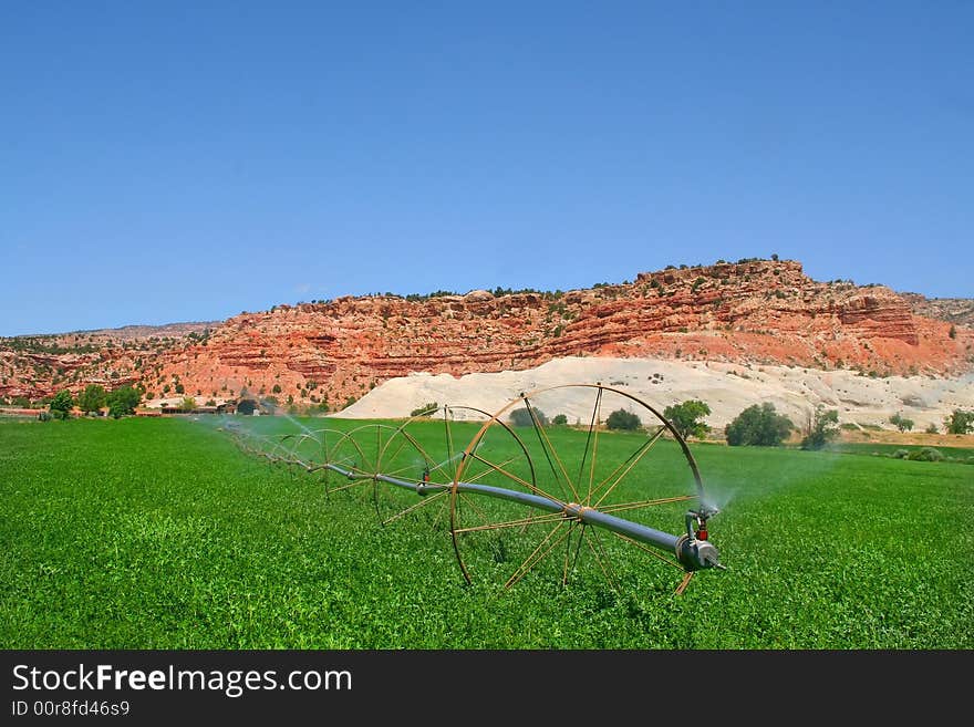 View of a farm in the  desert with hay in the foreground and a red rock mountain  in the background with blue sky�s and puffy clouds. View of a farm in the  desert with hay in the foreground and a red rock mountain  in the background with blue sky�s and puffy clouds