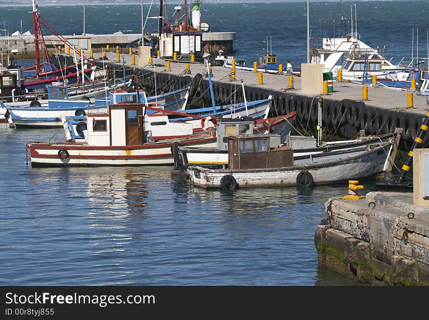 Fishing boats moored to the pier in Kalk Bay harbour, Cape Town, South Africa. The colourful boats are brightly reflected in the water of the harbour. Fishing boats moored to the pier in Kalk Bay harbour, Cape Town, South Africa. The colourful boats are brightly reflected in the water of the harbour.