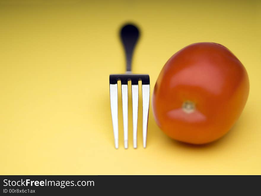 Fork and tomato on yellow