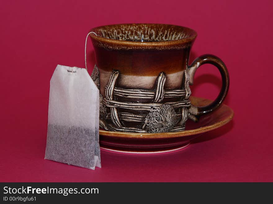 It is a an interesting cup with a tea bag on a red background. It is a an interesting cup with a tea bag on a red background