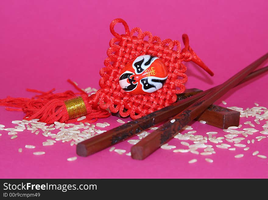 It is a Chinese traditional objects for food and decoration plus rice on a pink background. It is a Chinese traditional objects for food and decoration plus rice on a pink background