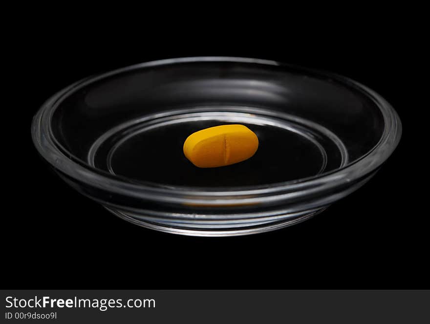 Yellow pill in bright glass saucer isolated on black