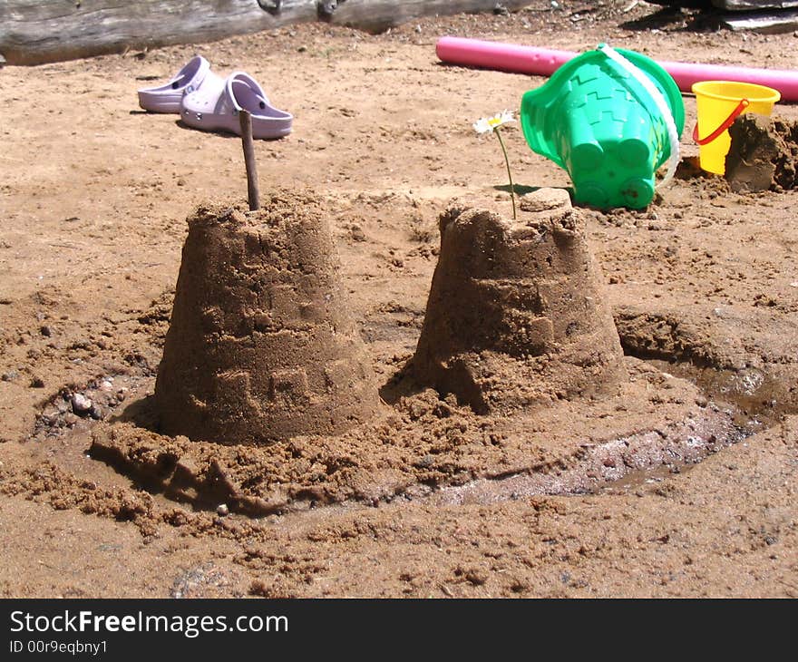 Sandcastle in the foreground with beach toys and shoes in background. Sandcastle in the foreground with beach toys and shoes in background