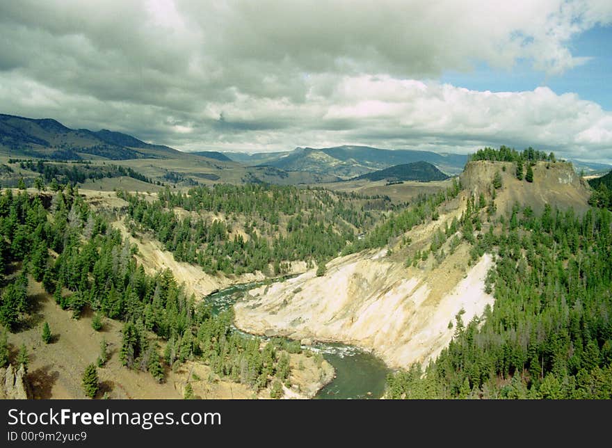 Yellowstone River snaking through the Yellowstone Grand Canyon. Stark canyon walls offer contrast to the green pines and blue summer sky.