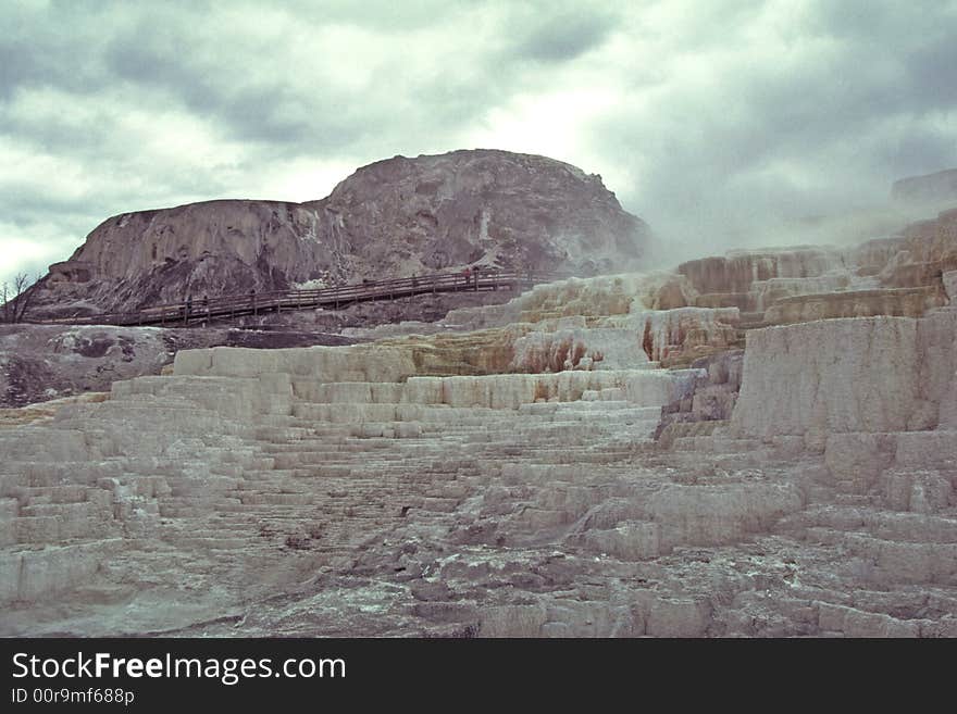 Steaming geothermal vents in Mammoth Hot Springs erupting from a landscape that resembles a moonscape. Geologic formations look like steps made of liquified stone.