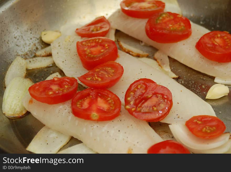 Three fish fillets in a frying pan with onions and tomatoes. Three fish fillets in a frying pan with onions and tomatoes